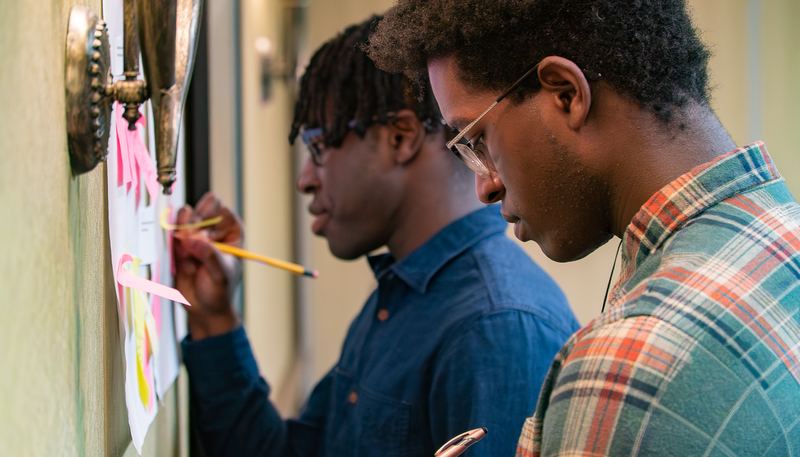 Two young participants add their reflections to a sticky-note wall